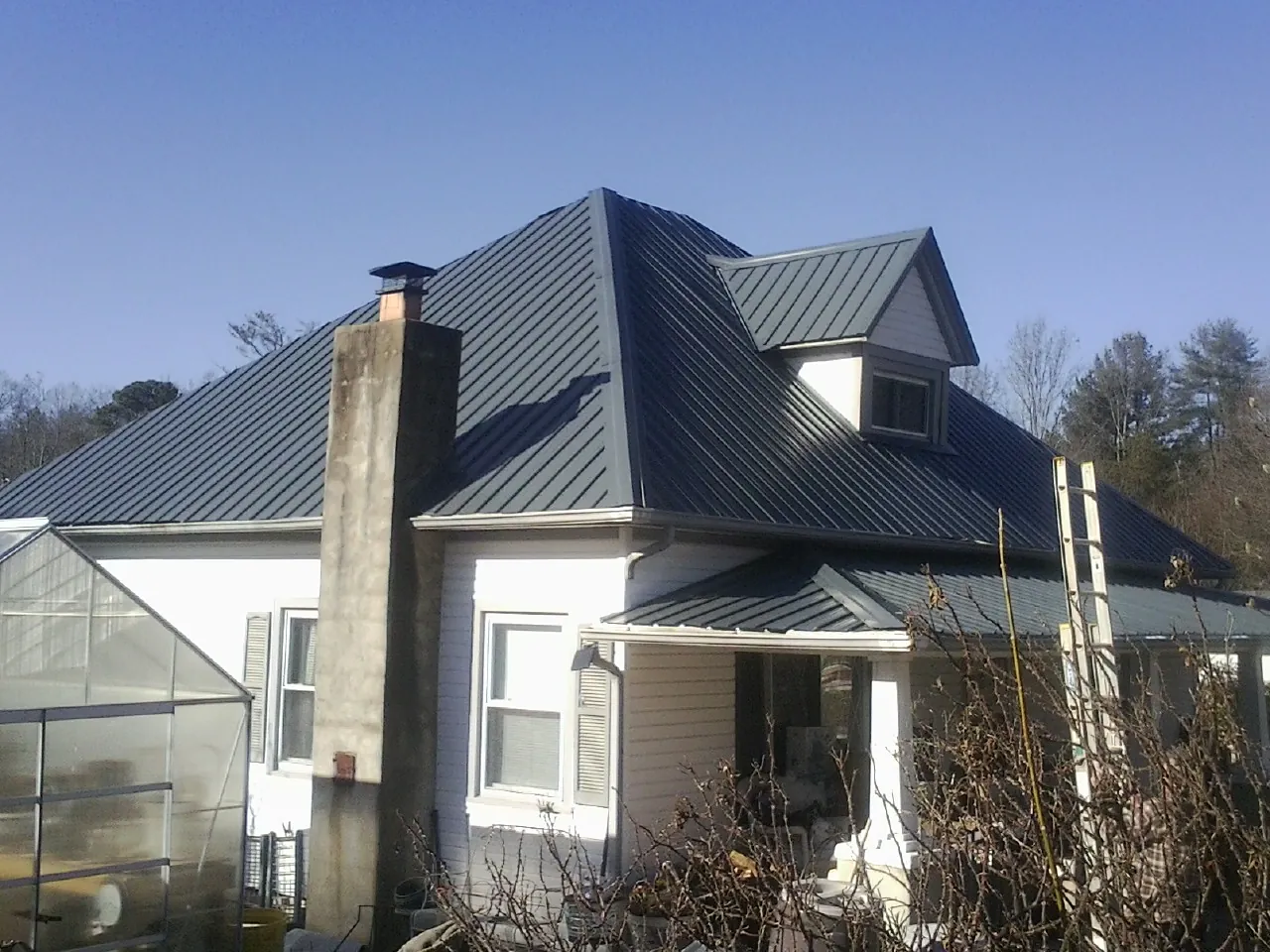 Dark blue standing seam metal roof on a white farmhouse with dormer — Slate & Tile Roof Repair by Roofing Brothers in Wellborn