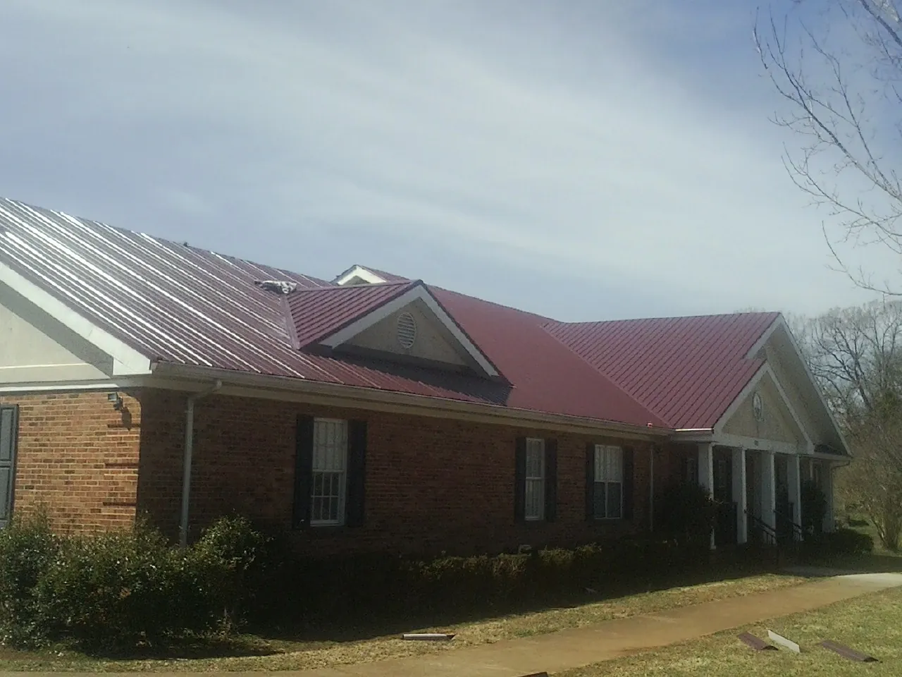 Red metal roof with gabled entries on a long brick building, from a Hail Damage Roof Repair job in Wellborn