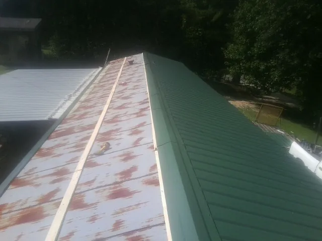 Old rusted panels beside newly installed green metal roofing — Wind Damage Roof Repair by Roofing Brothers in Wellborn
