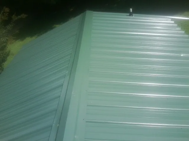 New green metal panels meeting at the ridge of a roof — Flat Roof Repair work by our crew in Wellborn