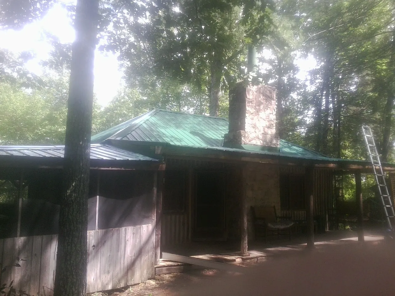 Green metal roof and stone chimney above a log cabin porch in Wellborn