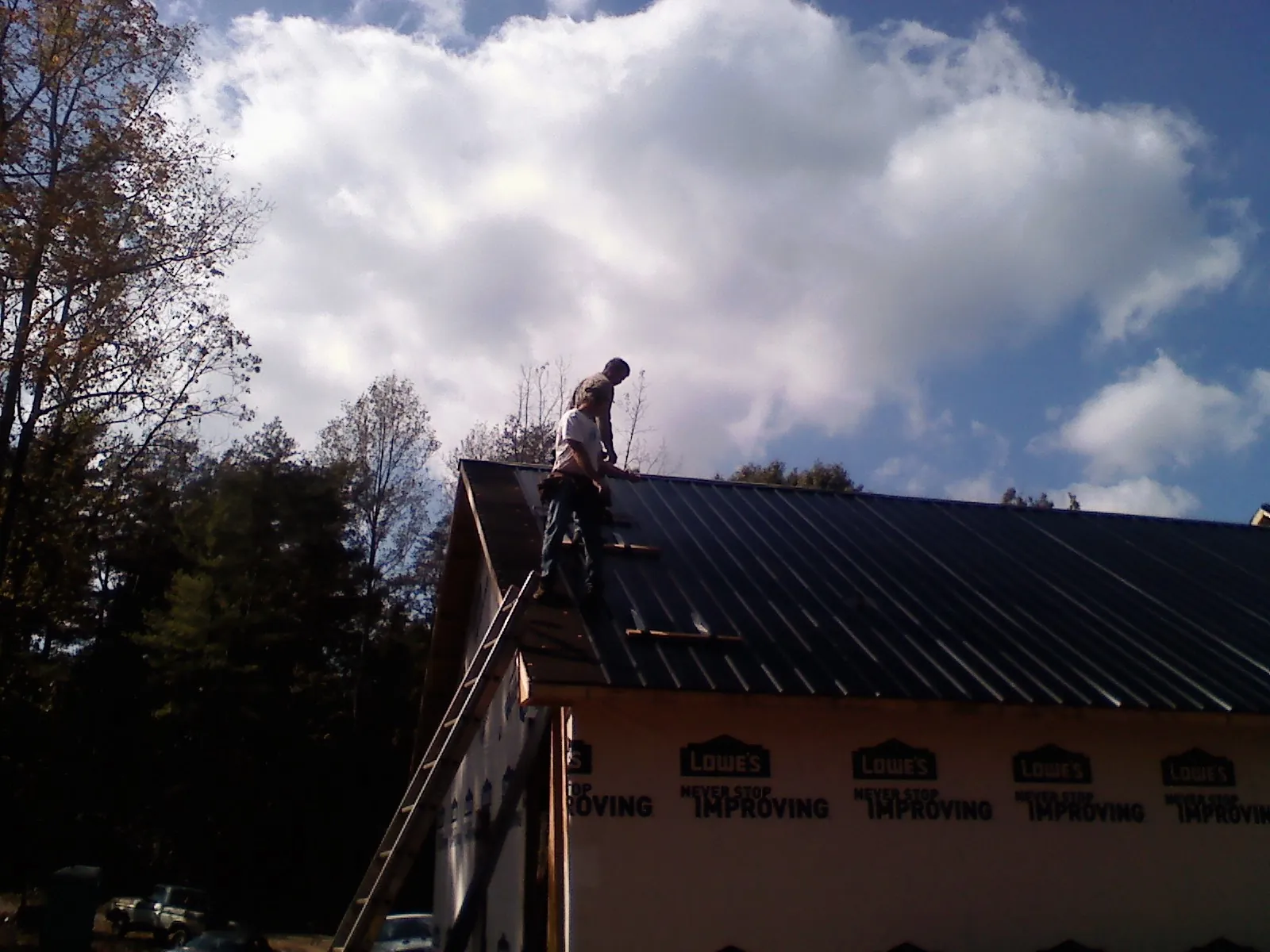Roofer fastening dark metal panels high against a cloudy sky, from a Roof Inspection job in Wellborn