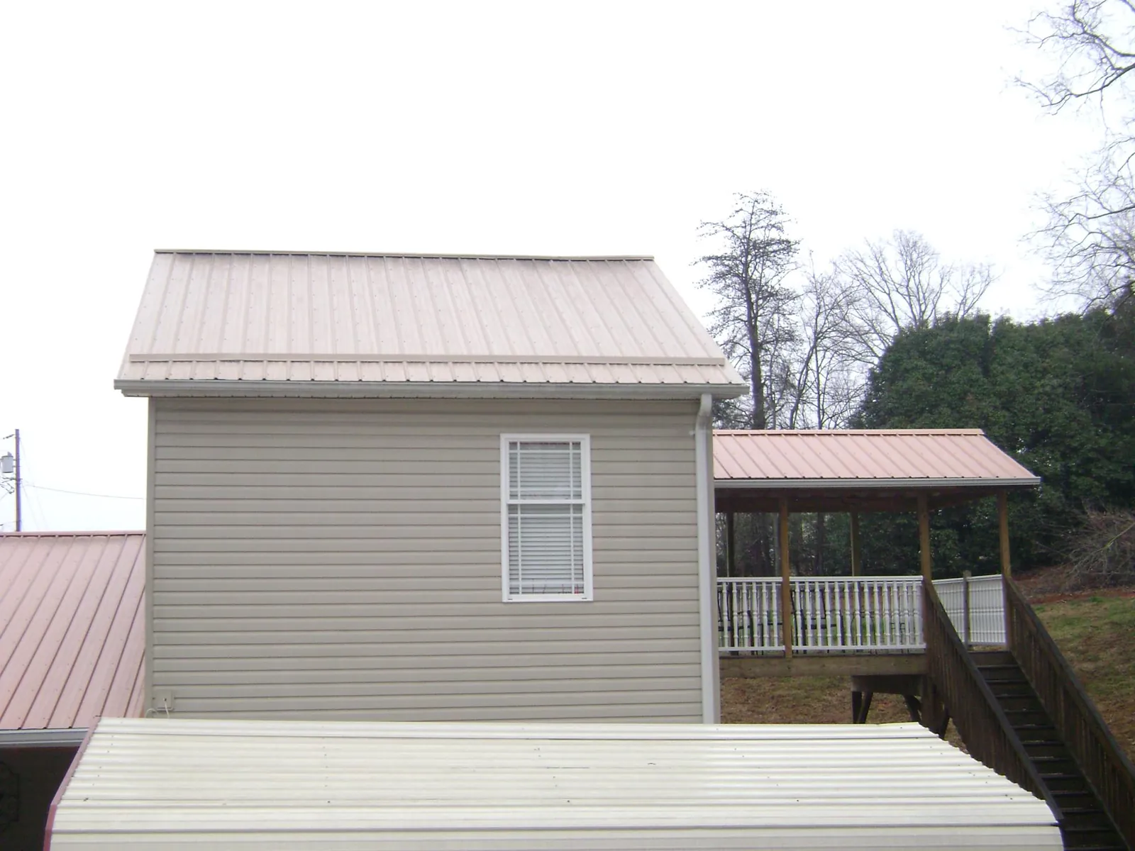 Tan metal roofs on a two story addition and attached porch, from a Roof Replacement job in Wellborn